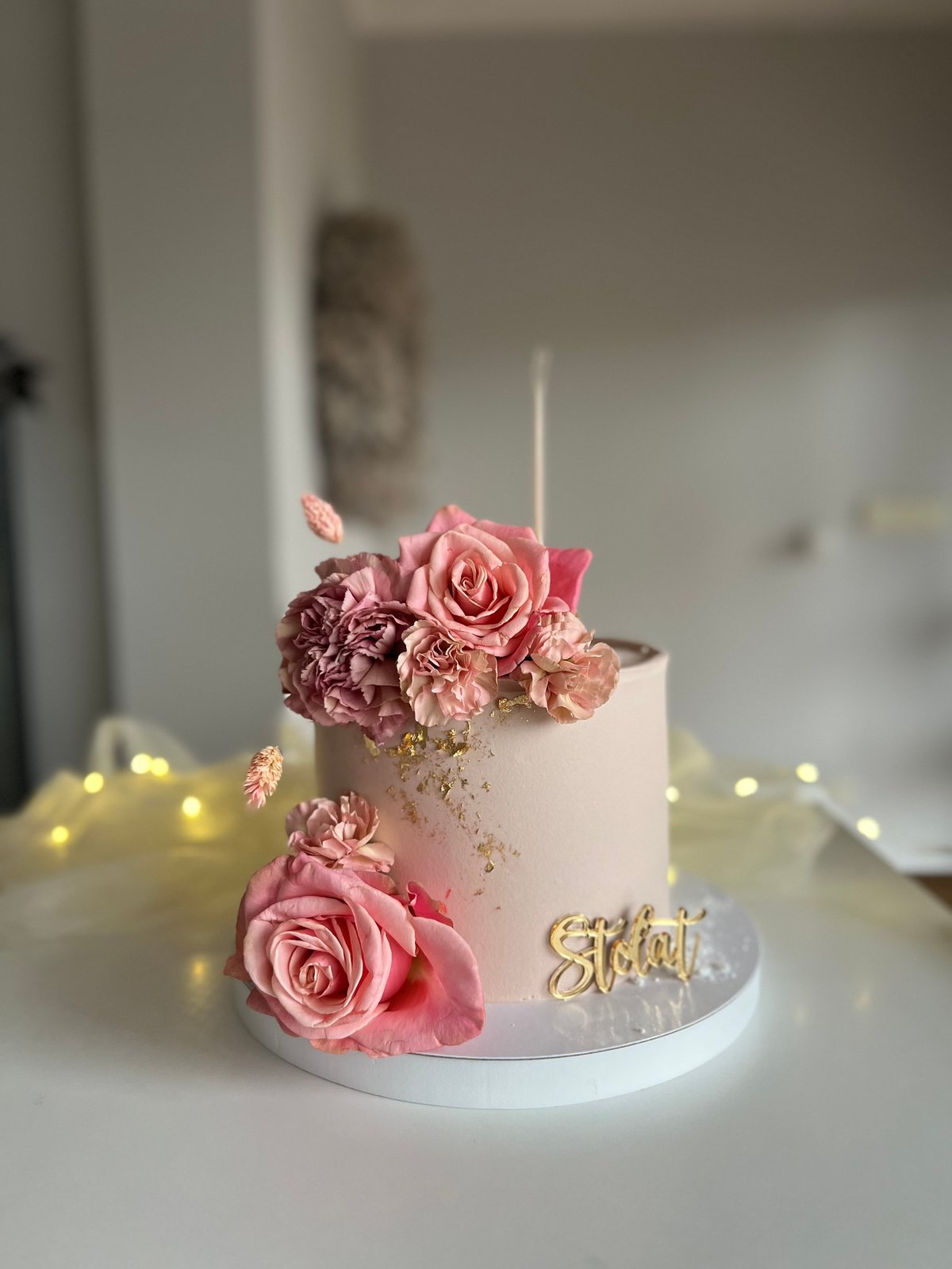 Elegant white cake decorated with pink and burgundy roses, gold sparkle details, and a gold Stylish topper on a white base