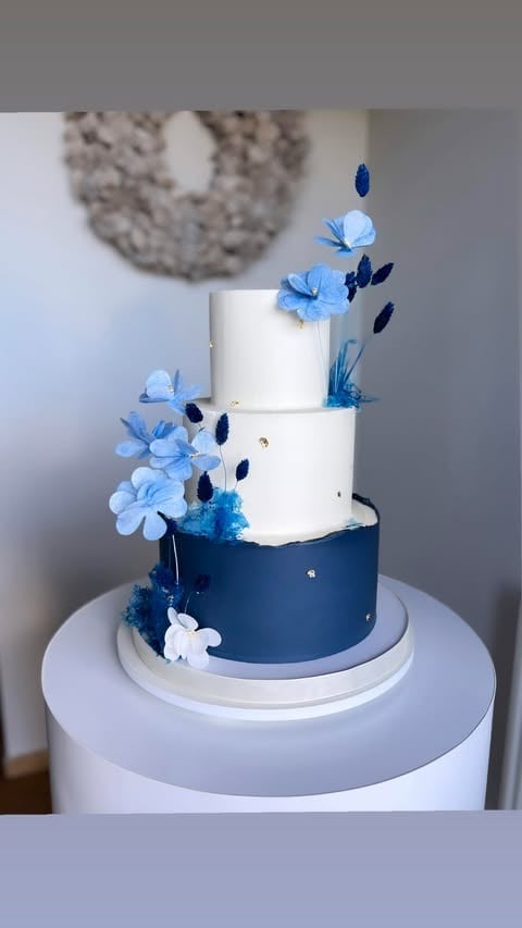 Multi-tiered wedding cake with white and navy blue tiers decorated with light blue flowers and blue leaves