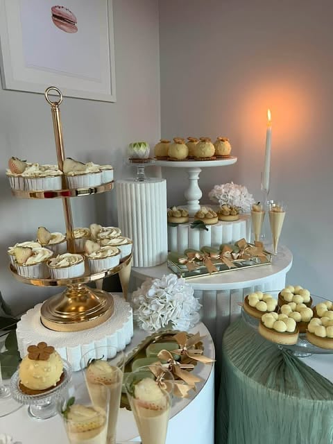 Elegant dessert display with tiered stands holding pastries, macarons, and cream desserts, decorated with candles and white flowers