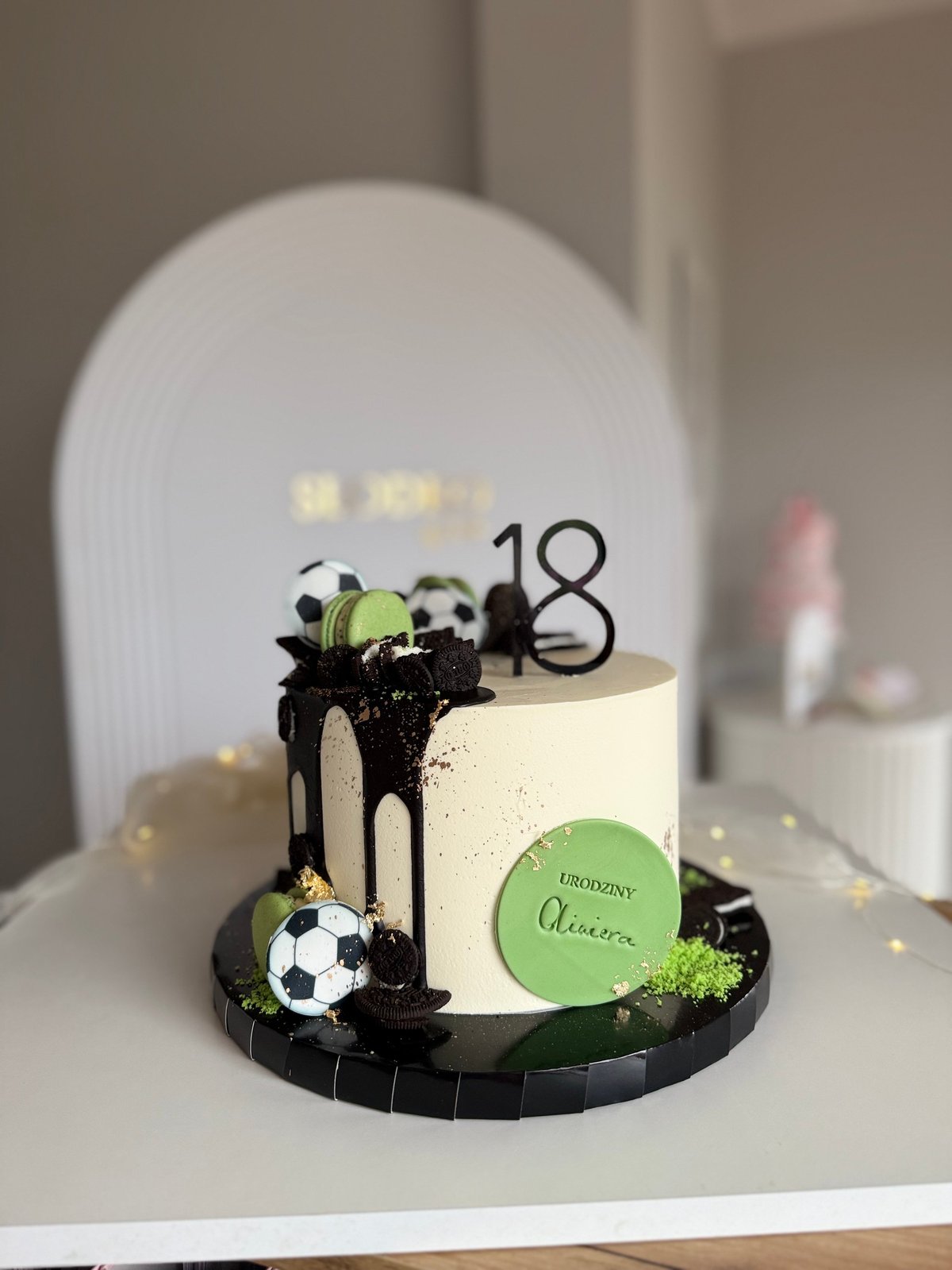 Birthday cake decorated with black drip, soccer ball toppers, green accents, and number 18 on a white plate