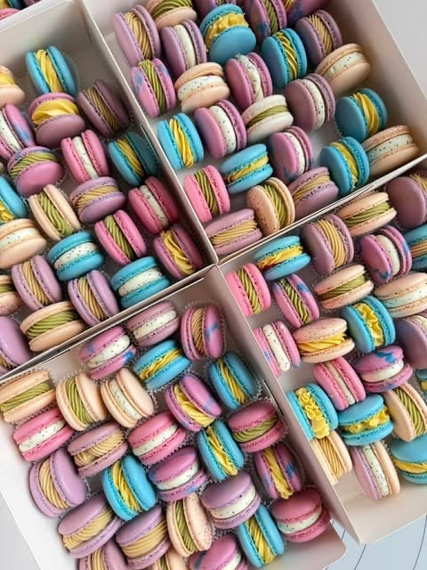 Assorted colorful macarons in white boxes, featuring pink, blue, yellow and cream flavored French pastries with piped details