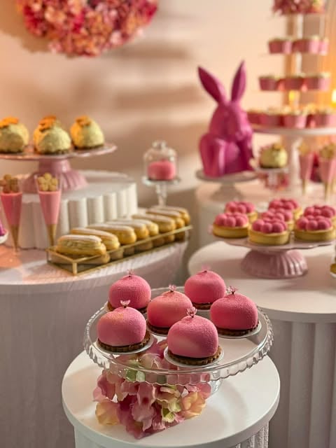 Elegant Easter celebration display with pink macarons, pastries, decorative bunny figurine, and floral arrangements on white tiered stands