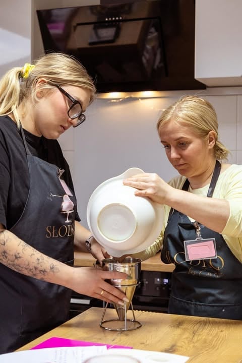 Two women in a kitchen examining a white ceramic bowl during what appears to be a culinary demonstration or workshop