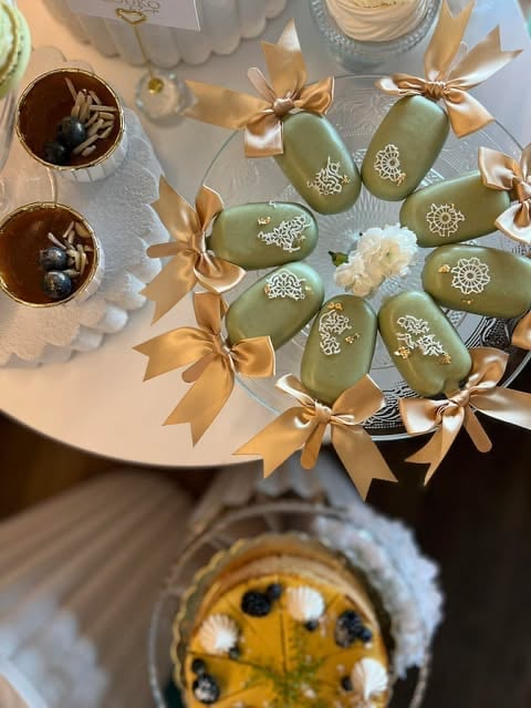 Overhead view of elegant desserts including green-frosted Easter eggs with gold ribbons, chocolate tarts, and a fruit tart on white serving plate