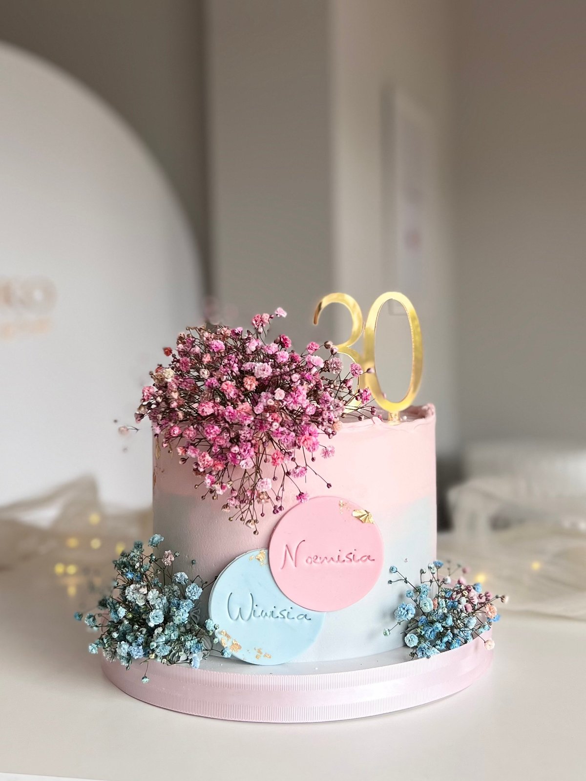 Pastel pink and blue 30th birthday cake decorated with dried babys breath flowers and gold number toppers