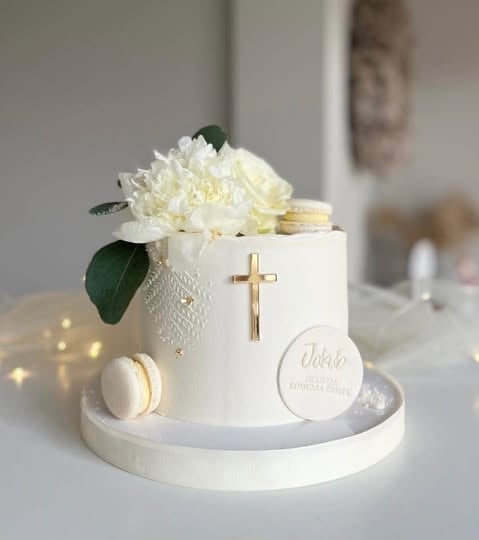 Elegant white tiered cake with gold cross, fresh white flowers, macarons, and religious text decoration on white base