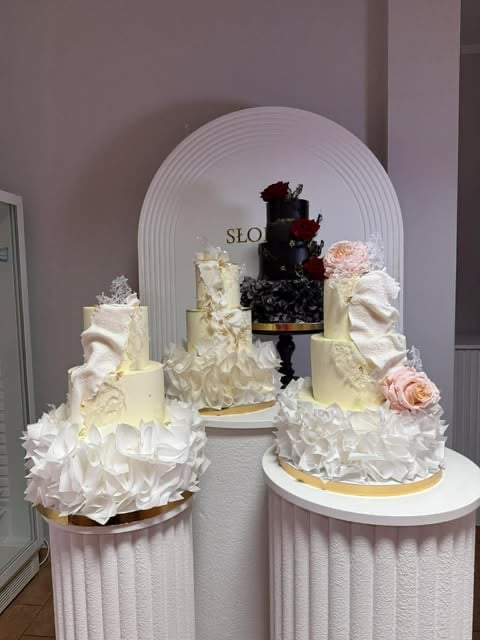 Display of four elegant tiered wedding cakes with white frosting, one with black berries, arranged on pedestals under an arched backdrop