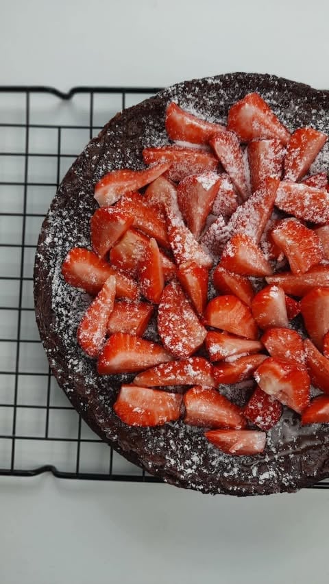 Chocolate cake topped with fresh strawberries and powdered sugar on a cooling rack