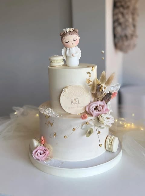 Three-tiered white wedding cake decorated with dried flowers, macarons, and a bride and groom figurine topper on a white stand