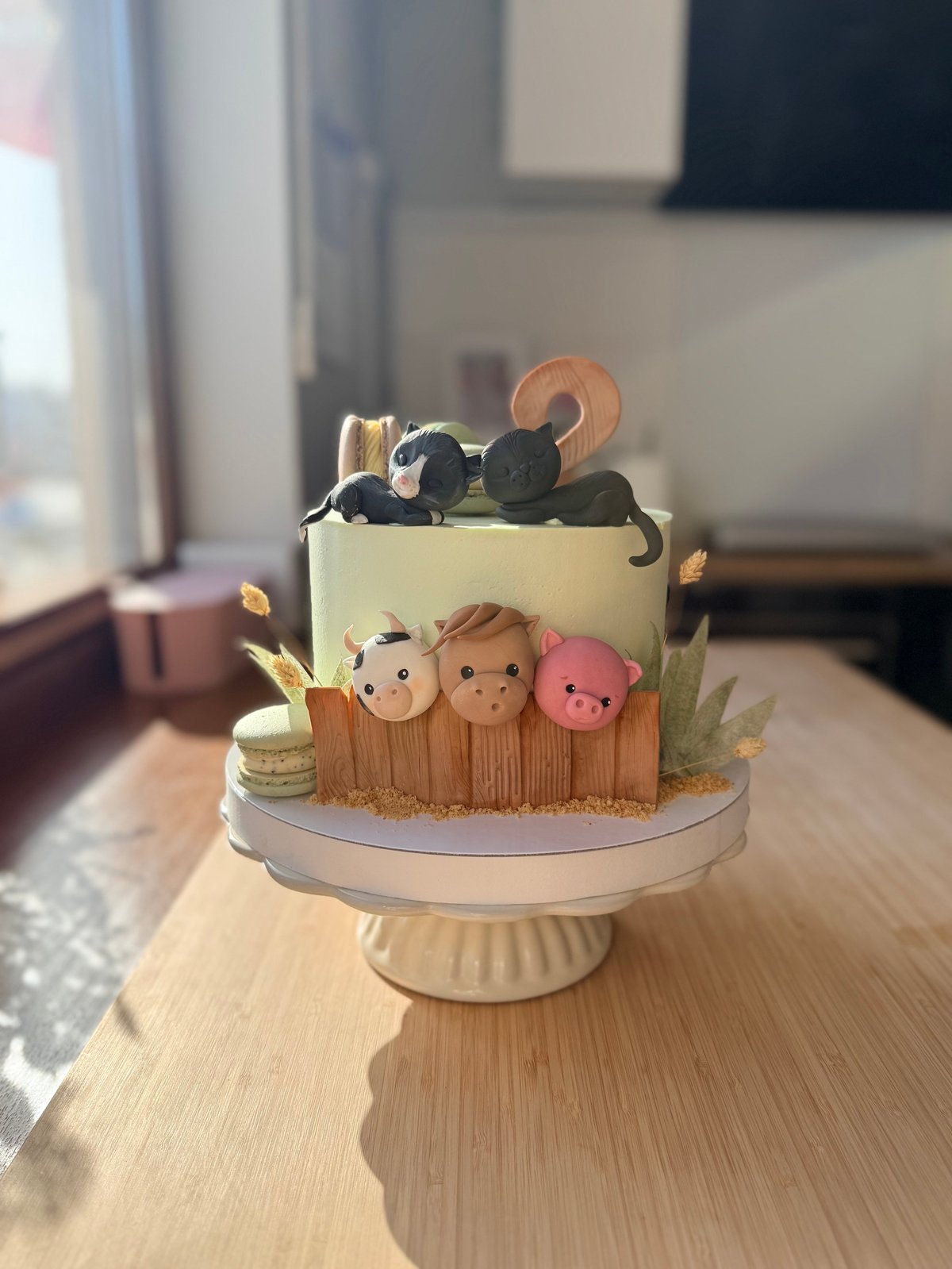 Two-tiered fondant cake with animal characters, wooden fence base, and number 2 topper on a beige cake stand