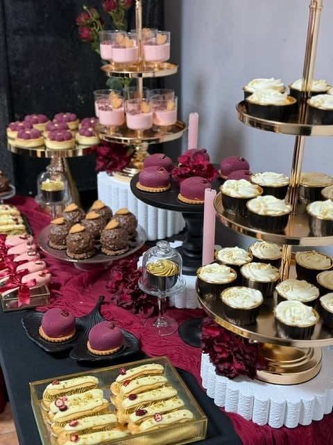 Elegant dessert display with burgundy and gold tiered stands featuring macarons, cupcakes, pastries, and decorative flowers