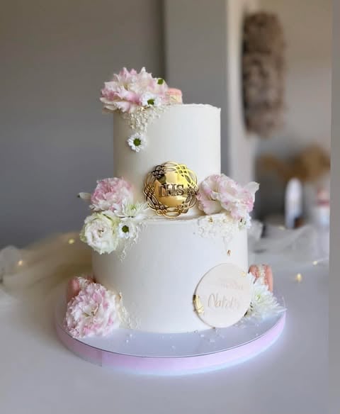 Three-tiered white wedding cake decorated with pink and white flowers, gold sphere accent, and a light pink base with illuminated bottom