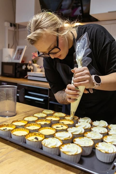Baker piping cream filling into tart shells on a baking tray in a professional kitchen