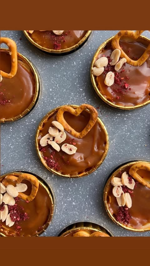 Multiple chocolate tarts with raspberry jam, sliced almonds, and heart-shaped cutouts arranged on a gray speckled surface