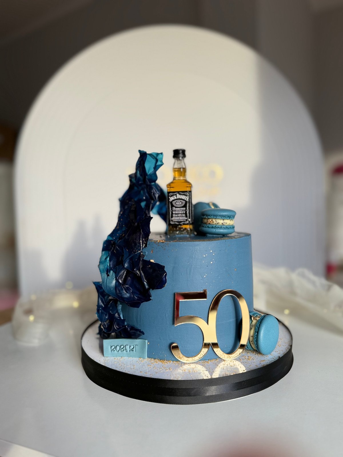 A 50th birthday cake with a blue bear figure, whiskey bottle, and gold 50 numeral on a black base
