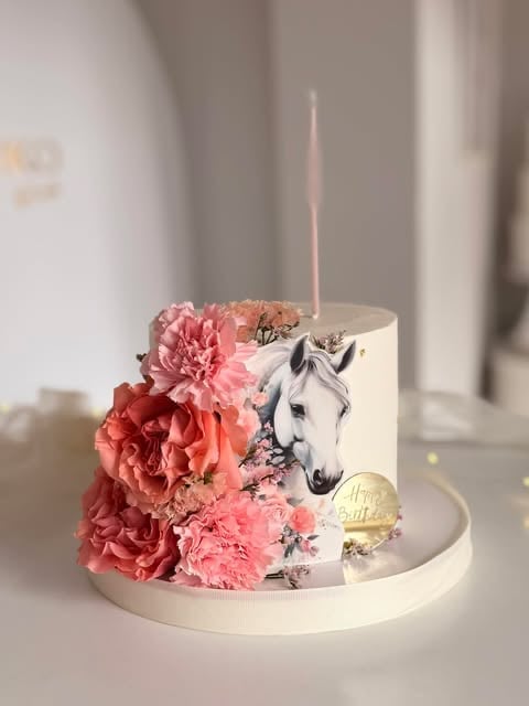 Elegant white birthday cake decorated with pink and coral peonies, horse illustration, and a pink candle on top
