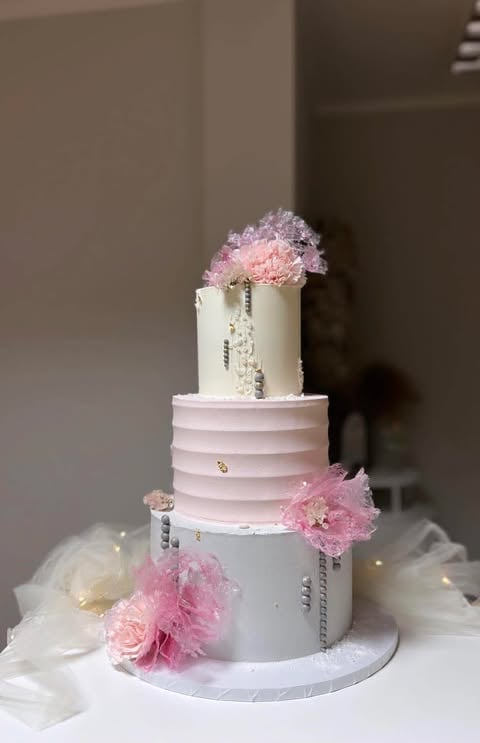 Three-tiered wedding cake with white and pink fondant layers, decorated with pink carnations and floral embellishments