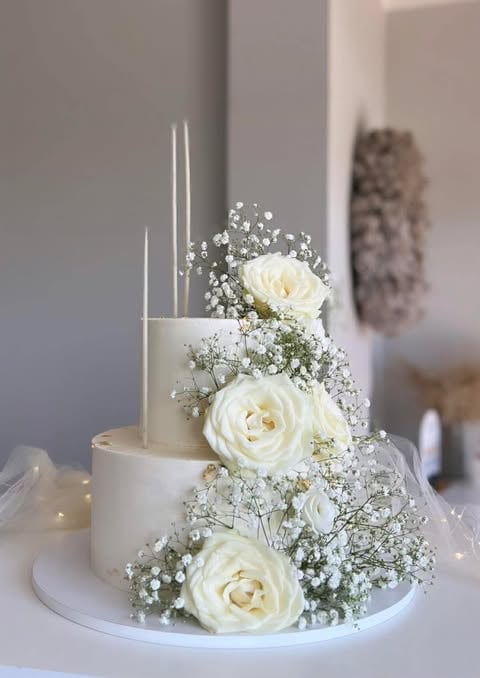 Three-tiered white wedding cake decorated with cream roses, babys breath, and tall silver candles