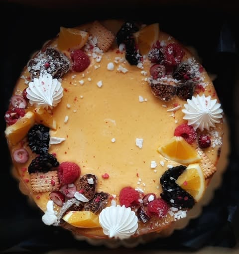 Gourmet dessert tart with yellow custard center, topped with fresh berries, candied fruit, pearl dust, and white cream decorations
