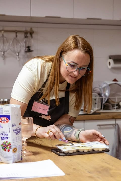 Woman in glasses and apron baking in a kitchen, decorating a tart with pastry tools and ingredients visible on the counter