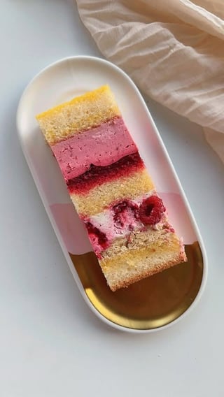 Layered cake slice on white oval plate with golden glaze and fresh raspberries
