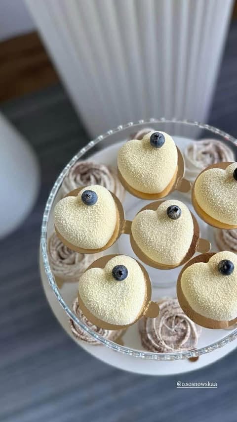 Overhead view of a clear container with heart-shaped desserts topped with gold sparkle and blueberries, arranged with chocolate swirls