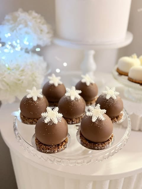 Chocolate sphere desserts decorated with white snowflakes on a crystal plate, displayed on a tiered white cake stand