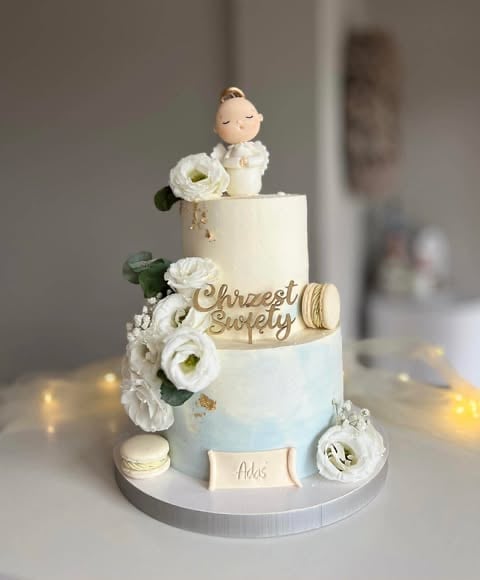 Elegant two-tiered wedding cake with white flowers, bride and groom cake toppers, gold accents, and Mr and Mrs tags on white base