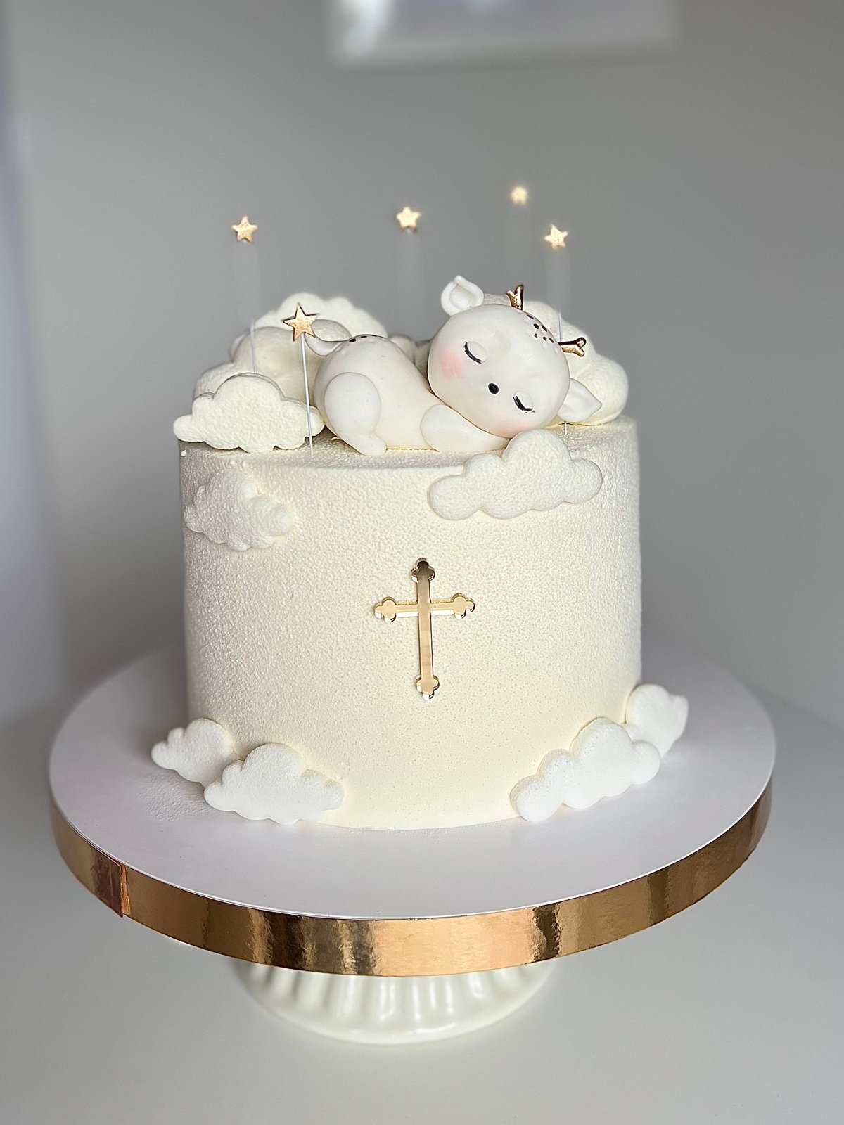 Elegant white christening cake decorated with a sleeping angel, clouds, golden cross, and star cake topper on a gold-rimmed stand