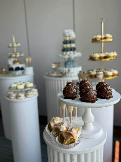 Elegant dessert display with white and gold tiered cake stands holding chocolate truffles, pastries, and decorative gold accents on gray background