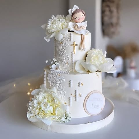 Elegant white tiered christening cake with religious cross, angel figurine, and white floral decorations