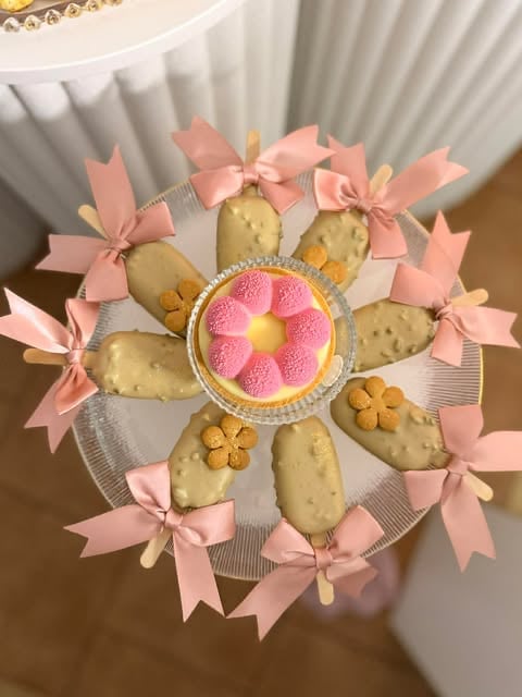 Decorative arrangement of shortbread cookies and candies with pink ribbons arranged in a flower pattern on white tulle fabric