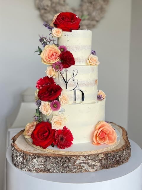Five-tier white wedding cake decorated with red, pink, and peach flowers on a rustic wooden base with Yes text