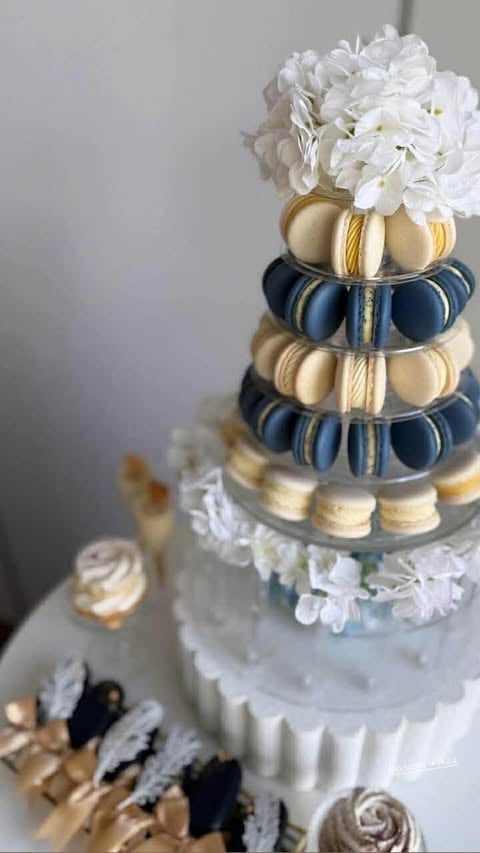 Elegant tiered wedding cake with white frosting, decorated with white flowers on top and macaron towers in cream and navy blue between layers