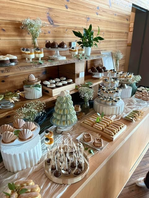 Elegant dessert table display with pastries, cakes, flowers, and macarons arranged on wooden shelves and surfaces