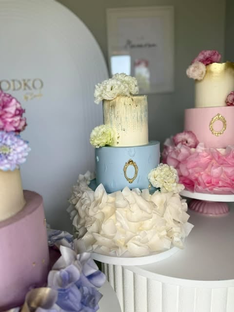 Display of elegant multi-tiered wedding cakes decorated with fresh flowers, cream textures, and gold accents in pastel colors