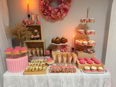 Pink and gold dessert table display with cupcakes, macarons, pastries, candles, and floral wreath decorations