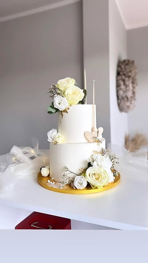 Two-tier white wedding cake with cream and yellow roses, babys breath, and a gold base on a white table