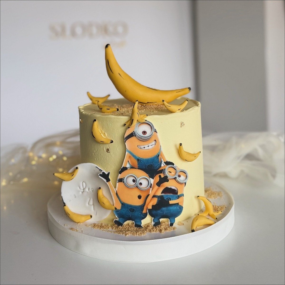 Decorated cake with Minion characters and banana theme, topped with fresh bananas and edible banana decorations