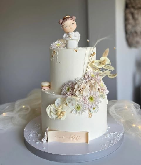 Two-tiered white wedding cake with floral decorations, a bride and groom cake topper, and gold accents on a silver cake stand