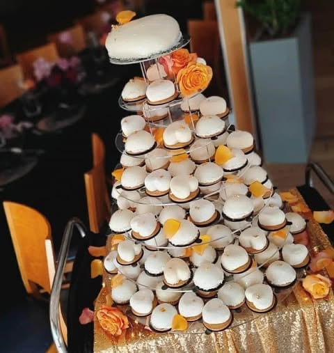 Tiered tower of cream-colored macarons stacked on a gold tablecloth, decorated with orange and yellow flowers