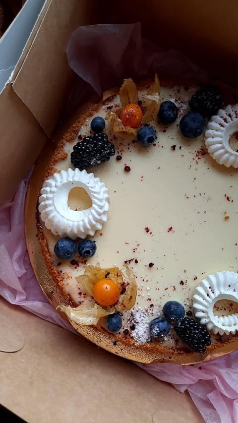 Creamy cheesecake decorated with fresh blueberries, blackberries, physalis, and white meringue swirls on a cookie crust