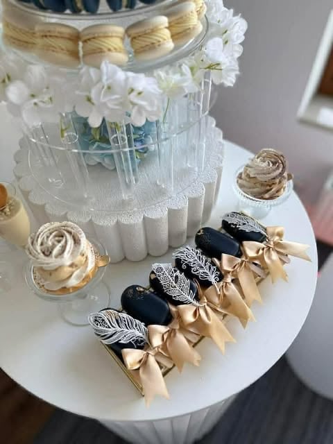 Elegant white tiered wedding cake with white flowers, gold ribbon, and decorative black and gold feather cake toppers on a white plate