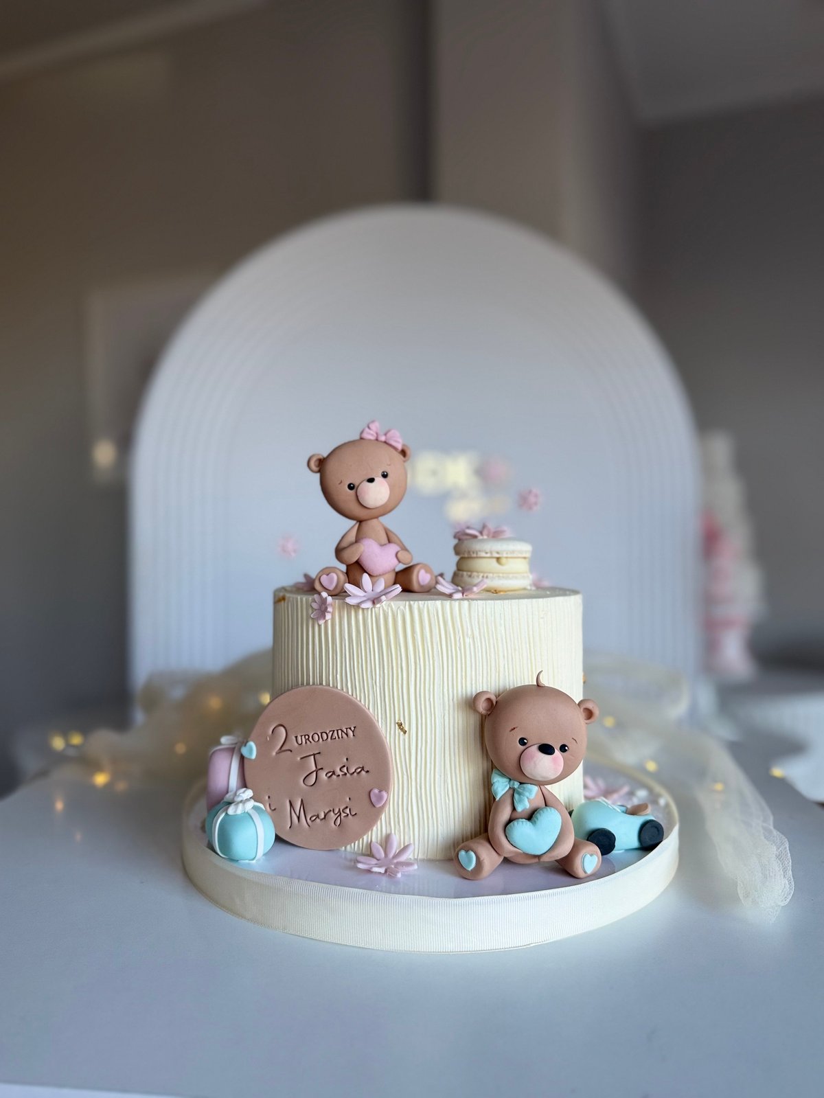 Pastel baby shower cake with fondant teddy bears, a decorative arch backdrop, and pink and blue accents