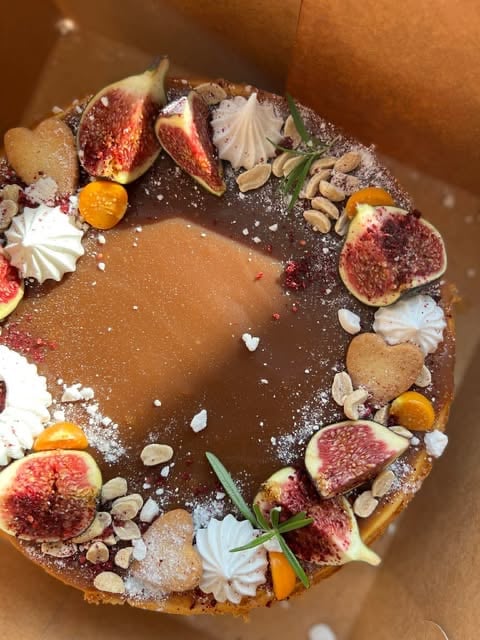 Chocolate tart decorated with fresh figs, nuts, edible flowers, and powdered sugar on brown paper