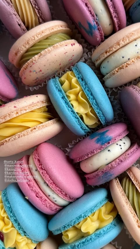 Assorted colorful French macarons with vibrant pink, blue, cream, and purple shells filled with yellow ganache and ruffled frosting