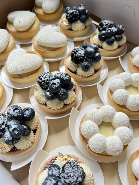 Assorted French pastries on white plates featuring cream puffs topped with fresh blueberries and powdered sugar, alongside vanilla and berry desserts