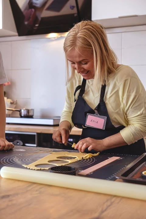 Woman wearing yellow cardigan and black apron with name tag preparing dough on kitchen counter