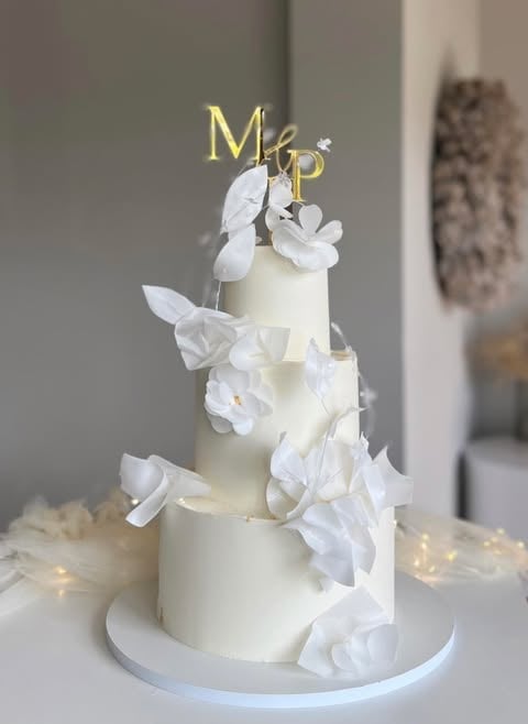 Three-tiered white wedding cake with white fondant flowers and gold Mr and Mrs topper