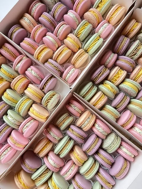 Assorted macarons in pink, yellow, green, and purple arranged in cardboard boxes